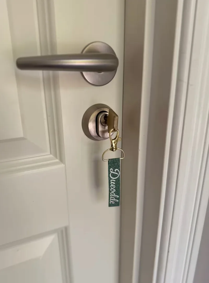 A brass key in the lock with a small green fabric keyring reading 'Dueodde'.