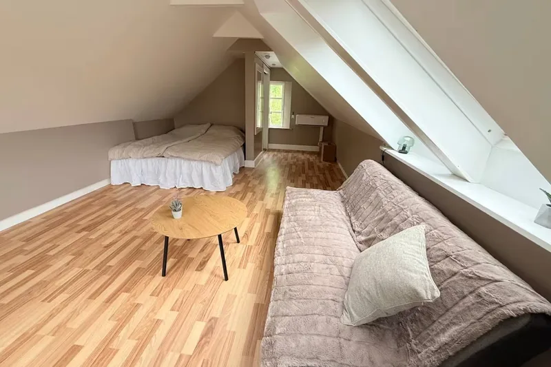 The Hammershus loft from inside — a wide attic with sloped white ceilings, a daybed under the skylight, light wood floors, and a small coffee table.