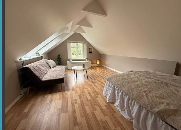The Hammershus Penthouse Room — an attic loft with white sloped ceilings and exposed beams, a double bed, a daybed, and a dormer window.