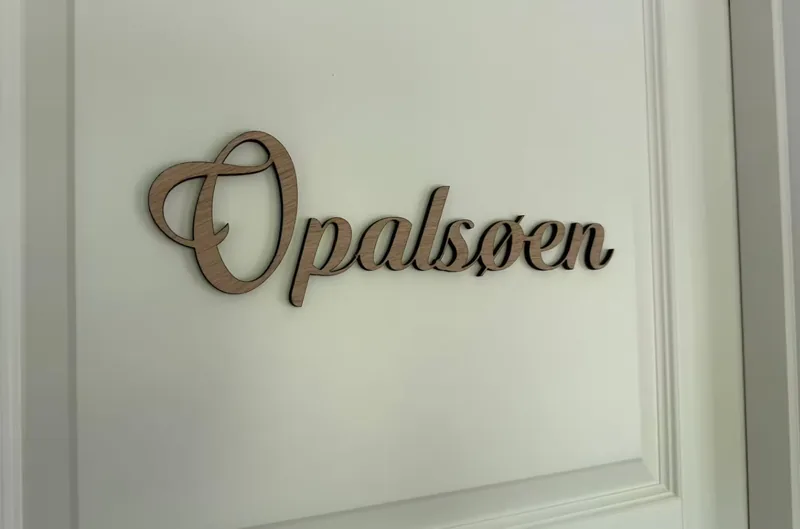 A wooden sign reading 'Opalsøen' in italics on the room's white panelled door.