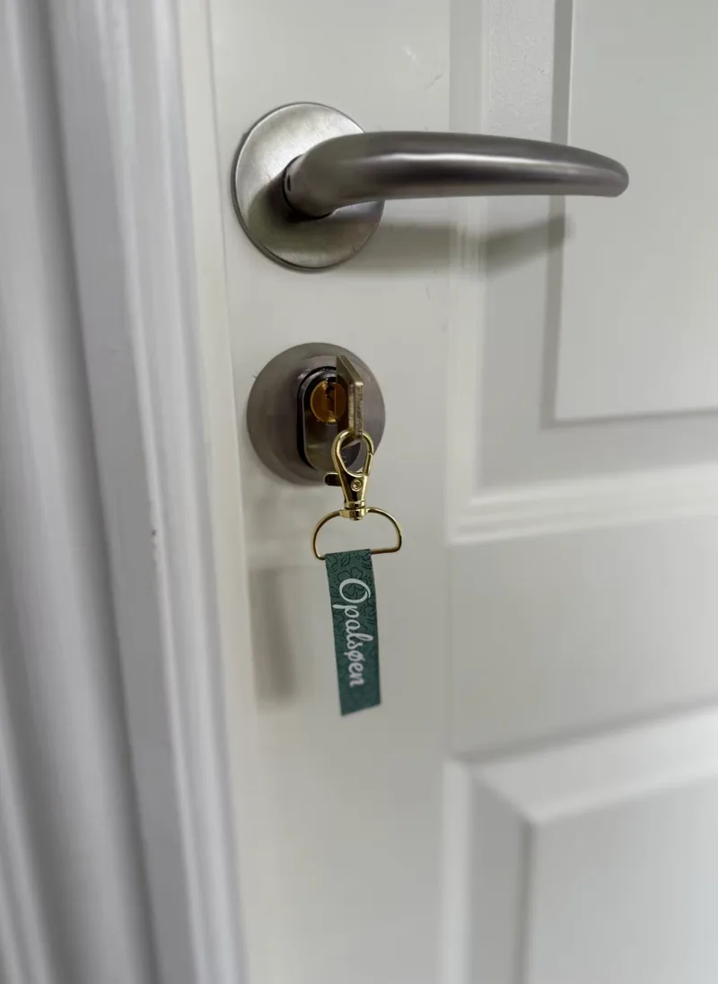 A brass key in the lock with a small green fabric keyring reading 'Opalsøen'.