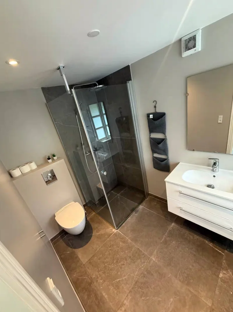 The shared bathroom — a walk-in stone-tiled shower, a white basin, and a wall-hung toilet.