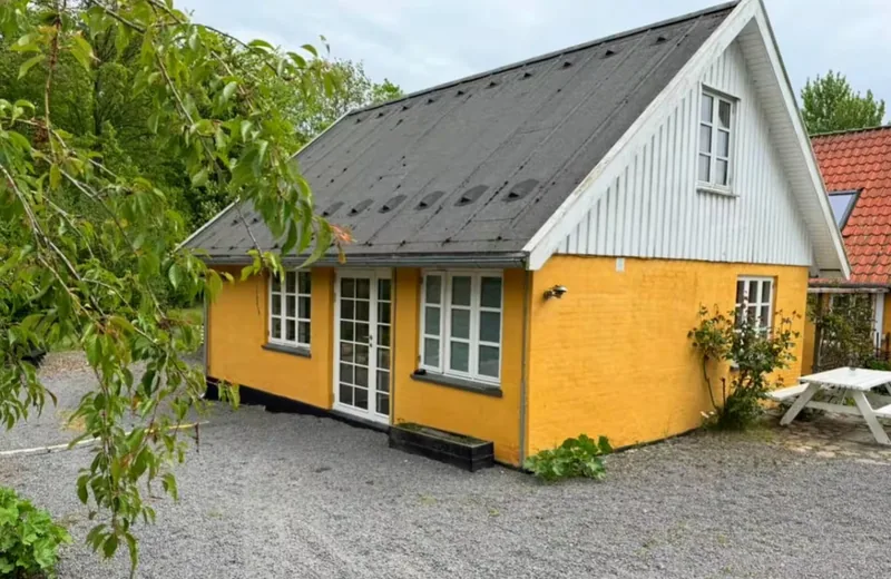 Krummeled's farmhouse — yellow lime-washed walls, a dark roof with skylights, a whitewashed gable, and a gravel courtyard.