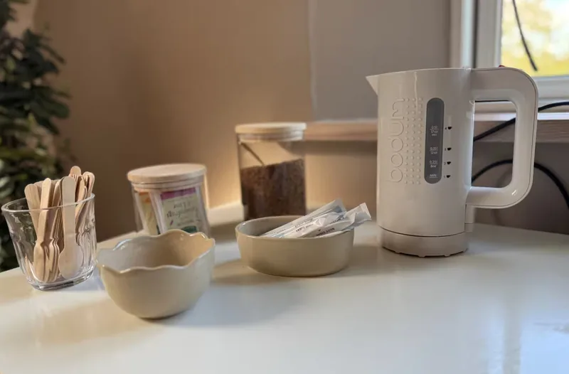 The tea and coffee station — a kettle, ceramic bowls of sugar sachets, a jar of coffee, and tea bags in a wooden holder.