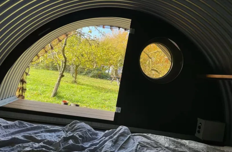 The shelter's wide opening onto the apple orchard in autumn colours, with a porthole alongside.